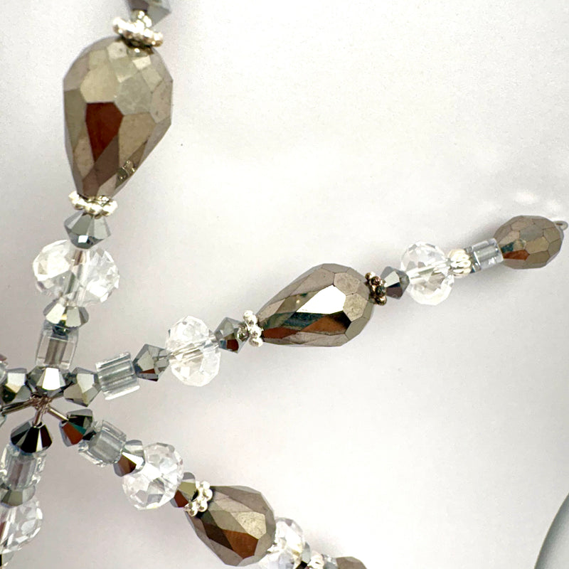 Close-up of a beaded jewelry strand featuring faceted brown teardrop beads, clear round crystal beads, and small metallic spacer beads on a white background.